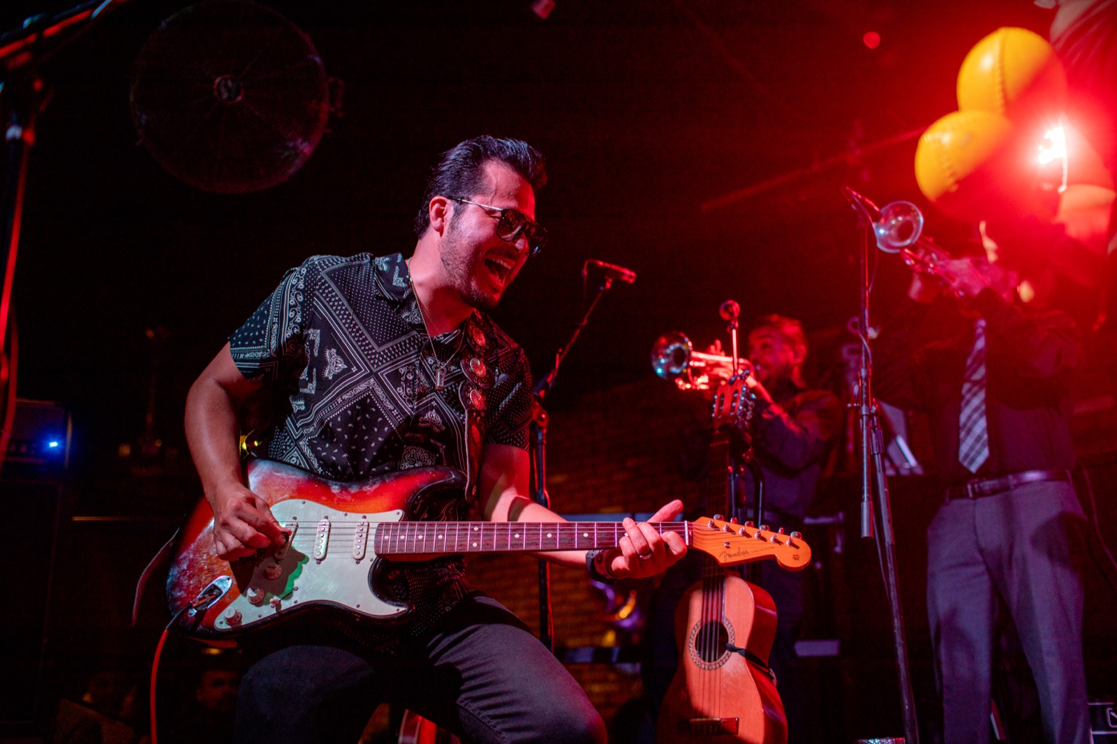 Carlos playing electric guitar onstage at Cellar Door under red stage lights